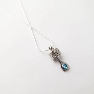 May include: A silver necklace with a silver piston pendant featuring a blue gemstone.