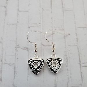 Peut inclure: Une paire de boucles d'oreilles argentées avec un motif de moteur rotatif noir et argent. Les boucles d'oreilles sont de style pendantes avec un crochet argenté.