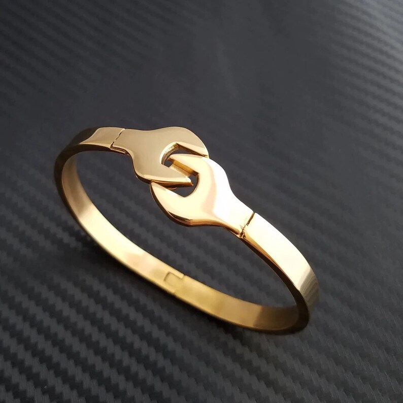Puede incluir: Una pulsera de tono dorado con un dise&ntilde;o de llave inglesa. La pulsera est&aacute; hecha de metal y tiene un acabado pulido.