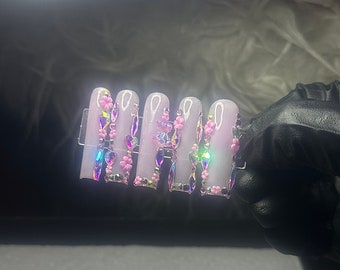 May include: Five pink press-on nails with iridescent rhinestones and pink flower accents.