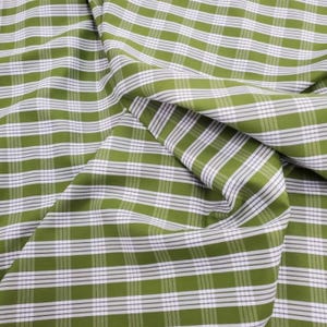 May include: Close-up of a green and white plaid fabric. The fabric has a classic grid pattern with alternating green and white stripes. The fabric is folded, showing the texture and drape of the material.