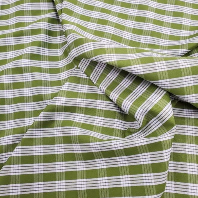 May include: Close-up of a green and white plaid fabric. The fabric has a classic grid pattern with alternating green and white stripes. The fabric is folded, showing the texture and drape of the material.