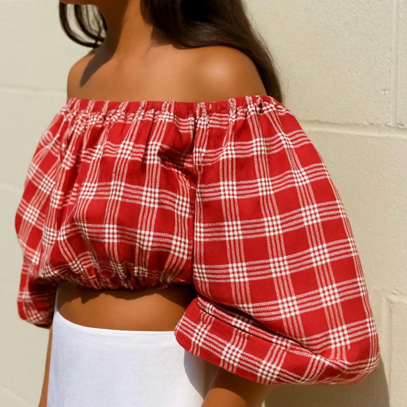 May include: Red and white plaid off-the-shoulder crop top. The top features a classic plaid pattern in red and white, with puffy sleeves and an elastic neckline. The crop top is made of a lightweight fabric.