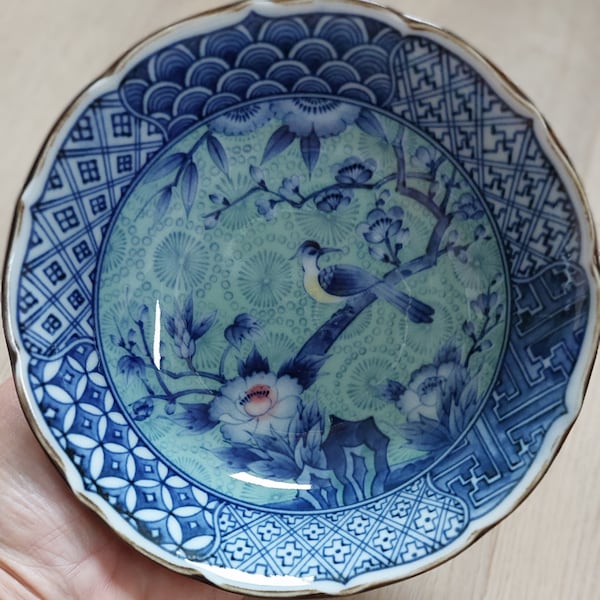 Prachtige vintage Chinese schaal met blauwe patronen en groene achtergrond met gele vogel en bloesemtakken met 1 roze bloem, golvende rand