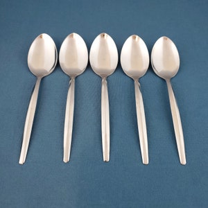 May include: Five stainless steel spoons arranged on a blue surface. Each spoon has a rounded bowl and a long, slender handle. The spoons are evenly spaced, creating a symmetrical pattern. The polished metal reflects light, highlighting their smooth surfaces. A simple, elegant design.
