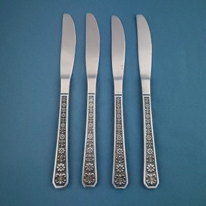 May include: Four stainless steel butter knives with a floral pattern on the handles. The blades are smooth and curved. The handles have a detailed design of flowers and geometric shapes.