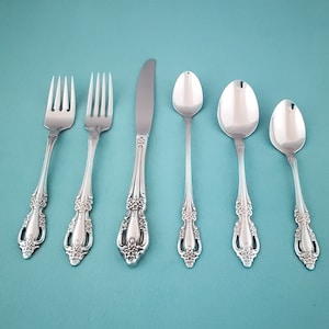 May include: A set of six silver-plated flatware pieces, including a knife, fork, and spoon. The pieces have ornate designs and are arranged on a light blue background.