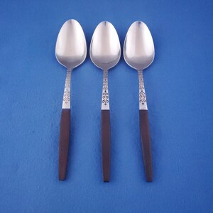 May include: Three silver spoons with dark brown handles. The spoons have a decorative pattern on the neck. The spoons are arranged vertically against a blue background. The spoons are likely for eating.