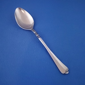 May include: A silver teaspoon with a decorative design on the handle. The spoon has a rounded bowl and a simple, elegant design.