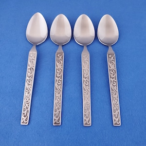 May include: Four stainless steel spoons with a floral engraved design on the handles. The spoons have a polished, reflective surface and are arranged on a blue background. The spoons are designed for serving.