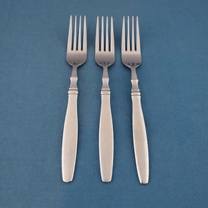 May include: Three stainless steel forks with a classic design, arranged on a blue background. Each fork features a long, smooth handle and four tines. The forks are ideal for a formal dining setting.