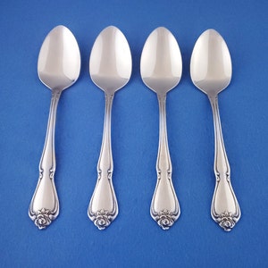 May include: Four silver spoons with a floral design at the base of the handle, arranged on a blue background. The spoons have a classic, elegant shape, reflecting light. The handles have a decorative, detailed pattern.