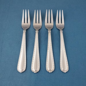 May include: Four silver forks with a decorative pattern on the handles. The forks have three tines and are arranged in a row against a blue background. The handles have a detailed, symmetrical design.
