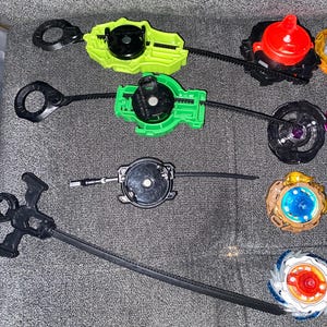 Puede incluir: Un surtido de lanzadores y peonzas giratorias de colores. Los lanzadores son verdes, amarillos y negros, con cuerdas de tracci&oacute;n. Las peonzas presentan detalles rojos, azules y dorados. Los juguetes est&aacute;n dise&ntilde;ados para el juego competitivo.