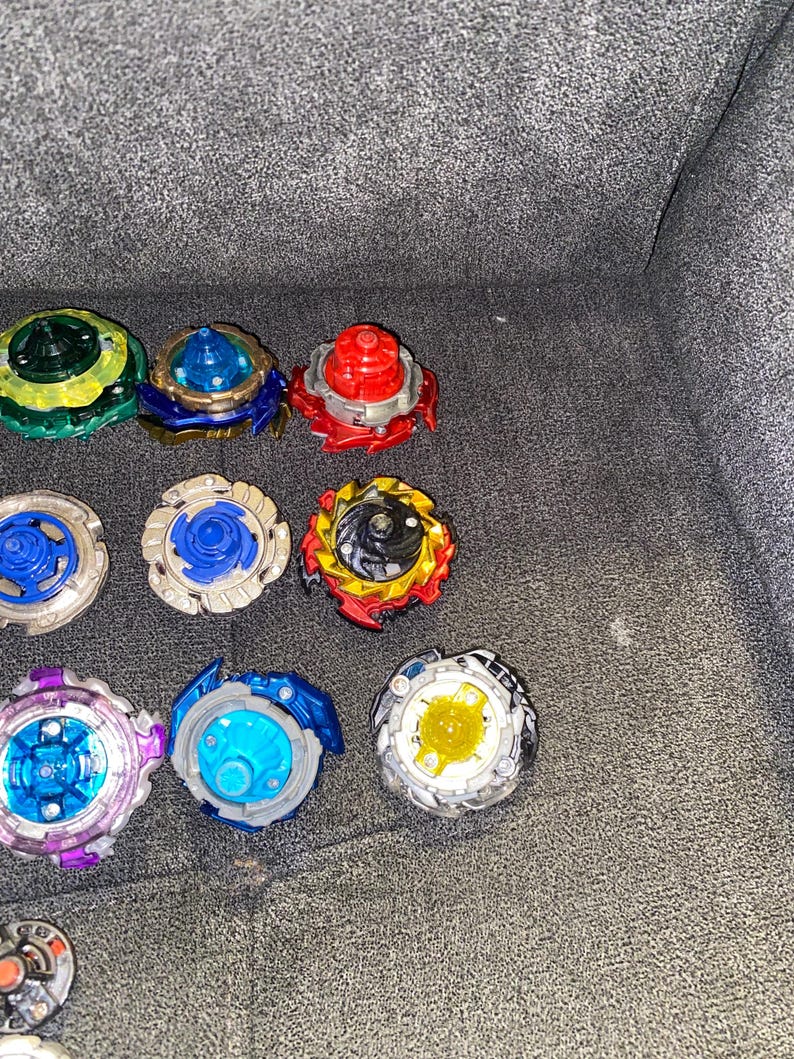 Puede incluir: Una colecci&oacute;n de coloridos trompos, incluyendo dise&ntilde;os verdes, azules, rojos y amarillos. Los trompos est&aacute;n dispuestos sobre una superficie gris, mostrando sus diversas formas y colores. Estos juguetes est&aacute;n dise&ntilde;ados para girar y competir.