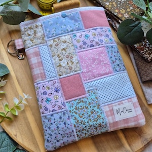 May include: A pastel patchwork tablet case with floral, dotted, and solid fabric squares. It has a button closure and a small keychain loop. The label "Mr. Cherie Designs" is visible on the lower right corner.
