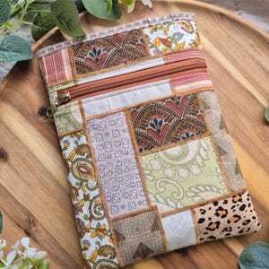 May include: A rectangular patchwork pouch with a brown zip. The pouch is made from various fabrics in brown, beige, and green, with floral, paisley, and geometric patterns. The pouch is a unique accessory.