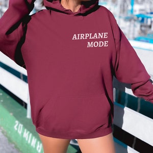 Puede incluir: Una sudadera con capucha color burdeos con un gr&aacute;fico bordado en blanco que dice "MODO AVI&Oacute;N".