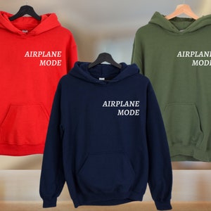 Puede incluir: Tres sudaderas con capucha en rojo, azul marino y verde oliva. Cada sudadera tiene el texto "AIRPLANE MODE" impreso en blanco en la parte delantera.