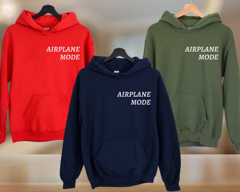 Puede incluir: Tres sudaderas con capucha en rojo, azul marino y verde oliva. Cada sudadera tiene el texto "AIRPLANE MODE" impreso en blanco en la parte delantera.