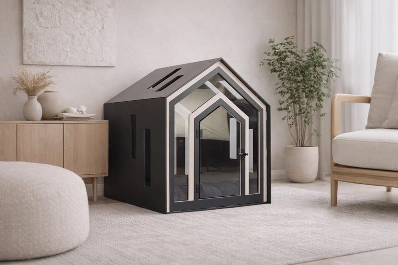 May include: A dark gray pet house shaped like a small cottage with a gabled roof, featuring a light-colored trim around the front door frame, a glass-paneled door with a black handle, and vertical rectangular cutouts on the side wall.