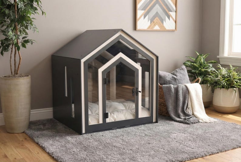 May include: A dark gray pet house with a gabled roof and a clear acrylic front panel featuring a white frame. The structure includes a hinged door with a black latch and a white tufted cushion inside for comfort, creating a secure enclosure.