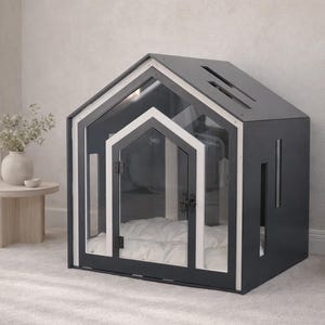 May include: A dark gray pet house with a gabled roof, featuring a clear acrylic front panel, a white-trimmed door frame, and a soft white tufted cushion inside. The structure includes vertical side cutouts and a slanted roof with rectangular vents.