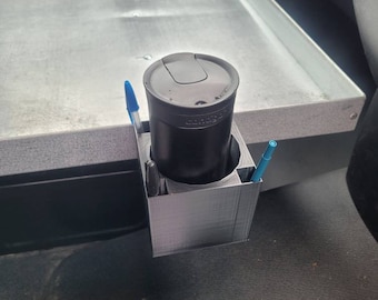 May include: A 3D printed car cup holder with a black travel mug and two blue pens inside.