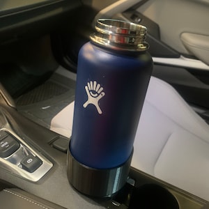 May include: A blue stainless steel water bottle with a black lid and a white logo is in a car cup holder.