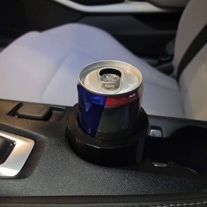 May include: A blue and red can of energy drink in a black cup holder in a car.