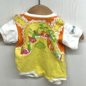 May include: A yellow, orange and white Cabbage Patch Kids t-shirt with a graphic of vegetables and the text "Cabbage Patch Kids".