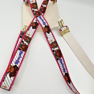 Peut inclure: Bretelles vintage avec un fond blanc, des bordures roses et un motif répété de poupées Cabbage Patch Kids. Les bretelles ont des clips en métal doré et une sangle élastique blanche.