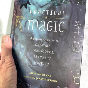 May include: A book titled "Practical Magic: A Beginner's Guide to Crystals, Horoscopes, Psychics & Spells" by Nikki Van De Car with illustrations by Katie Vernon. The cover features a watercolour background with stars, crystals, and a crescent moon.