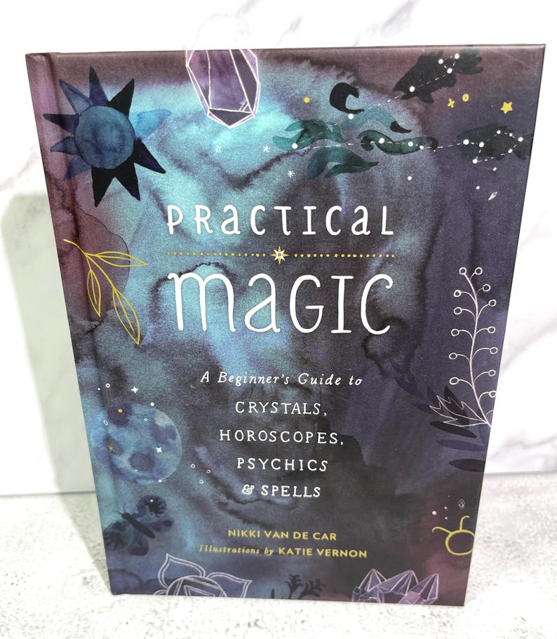May include: A book titled "Practical Magic: A Beginner's Guide to Crystals, Horoscopes, Psychics & Spells" by Nikki Van de Car with illustrations by Katie Vernon. The cover features a watercolour design with stars, moons, and crystals on a dark blue and purple background.