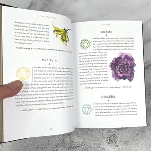 May include: A book open to a page about the Anahata chakra, the heart chakra. The page features a green watercolour illustration of a rose with a green and white mandala symbol. The text on the page reads "Anahata" and "The heart chakra is, of course, seated at the heart, but also at the lungs. This is the centre chakra, and is responsible for maintaining the balance between the other six. And how else could we achieve that balance but with love? By love we mean romantic love, self-love, friendship, kindness, compassion, and respect."