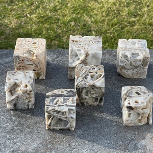 May include: Seven small, white, cube-shaped, natural stone paperweights with brown and gray markings. The cubes are arranged on a gray surface.