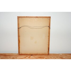May include: The back of a framed picture with a light brown wooden frame. The picture is hanging on a white wall.