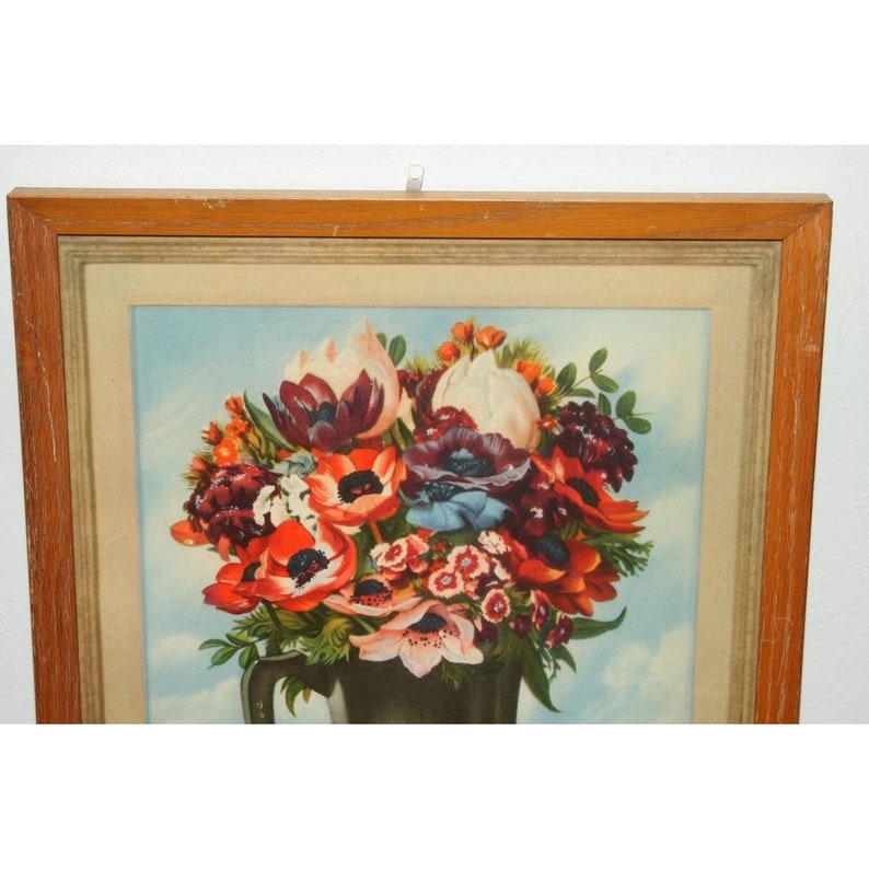 May include: A framed vintage print of a still life featuring a bouquet of red, white, and purple flowers in a green vase. The flowers are arranged in a symmetrical pattern and are surrounded by green leaves. The background is a light blue.