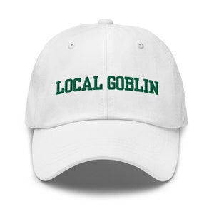 May include: White baseball cap featuring the embroidered text "LOCAL GOBLIN" in green. The cap has a curved peak and a button on top. A casual accessory.