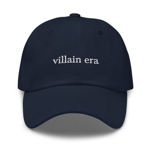May include: A navy blue baseball cap with the text "villain era" embroidered in white on the front.
