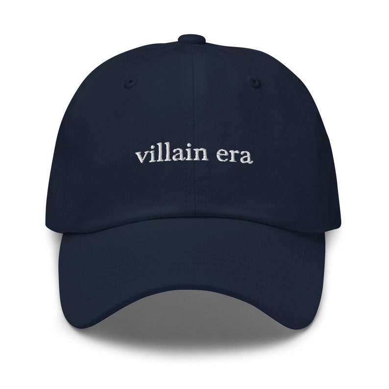 May include: A navy blue baseball cap with the text "villain era" embroidered in white on the front.
