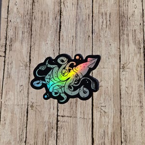 May include: A holographic sticker featuring a black and white illustration of a squid wrapped around a 20-sided die.