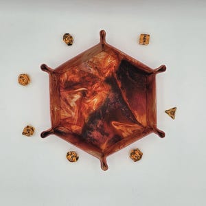 May include: A hexagonal dice tray with a swirling brown, orange, and white pattern. The tray is made of felt and has a leather-like texture. Six dice are scattered around the tray.