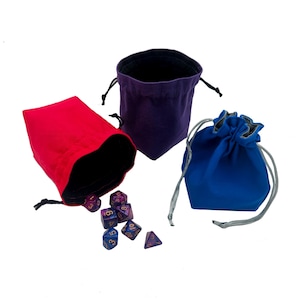 May include: Three velvet dice bags in red, purple, and blue, each with a drawstring closure. A set of polyhedral dice spills from the red bag. The bags are designed for tabletop gaming.