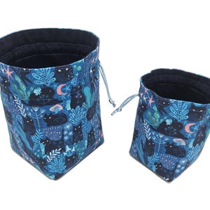 May include: Two blue drawstring bags with a black cat and foliage print. The larger bag is taller and wider than the smaller bag.