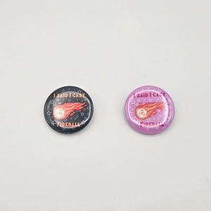 May include: Two round buttons with the text "I SAID I CAST FIREBALL" and a fireball graphic. One button is black with white text and a red and orange fireball. The other is light purple with white text and a red and orange fireball.