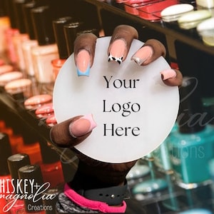 May include: A hand with manicured nails holds a white circular sign with the text "Your Logo Here." The nails feature various designs, including French tips with pink, blue, and silver accents. Nail polish bottles are visible in the background.