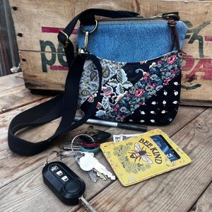 May include: A crossbody bag with a blue denim top and a quilted patchwork bottom featuring floral and paisley patterns. A yellow card holder with a bee illustration and the text BEE KIND, a black car key fob, and metal keys are included.