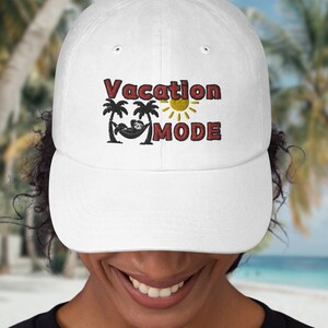 以下が含まれることがあります： 白い野球帽に、赤い刺繍で「Vacation Mode」と刺繍され、ヤシの木と太陽のグラフィックが描かれています。