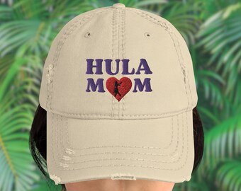 Puede incluir: Una gorra de béisbol desgastada de color beige con el texto "HULA MOM" bordado en morado con un corazón rojo y una silueta de una bailarina de hula dentro del corazón.